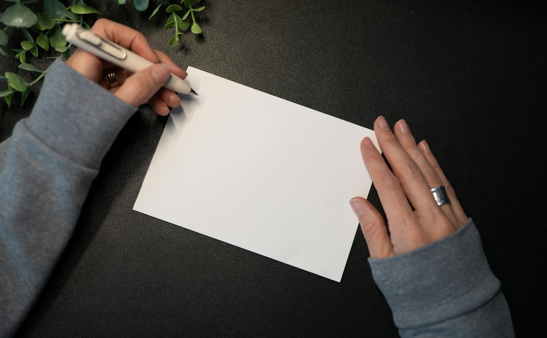 Hands about to write on a blank card on a dark desk